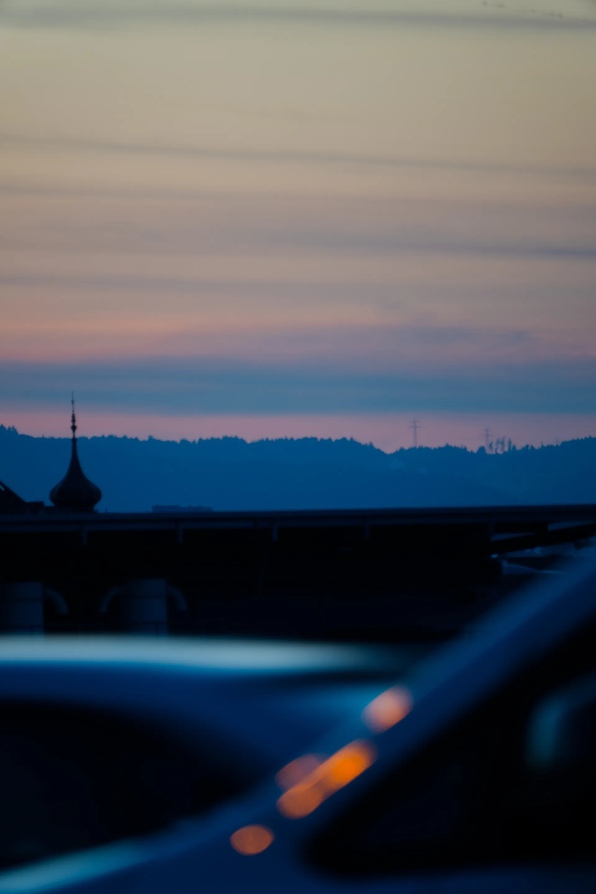 Blurred lights in the foreground frame a distant tower silhouette against the blue hour sky.