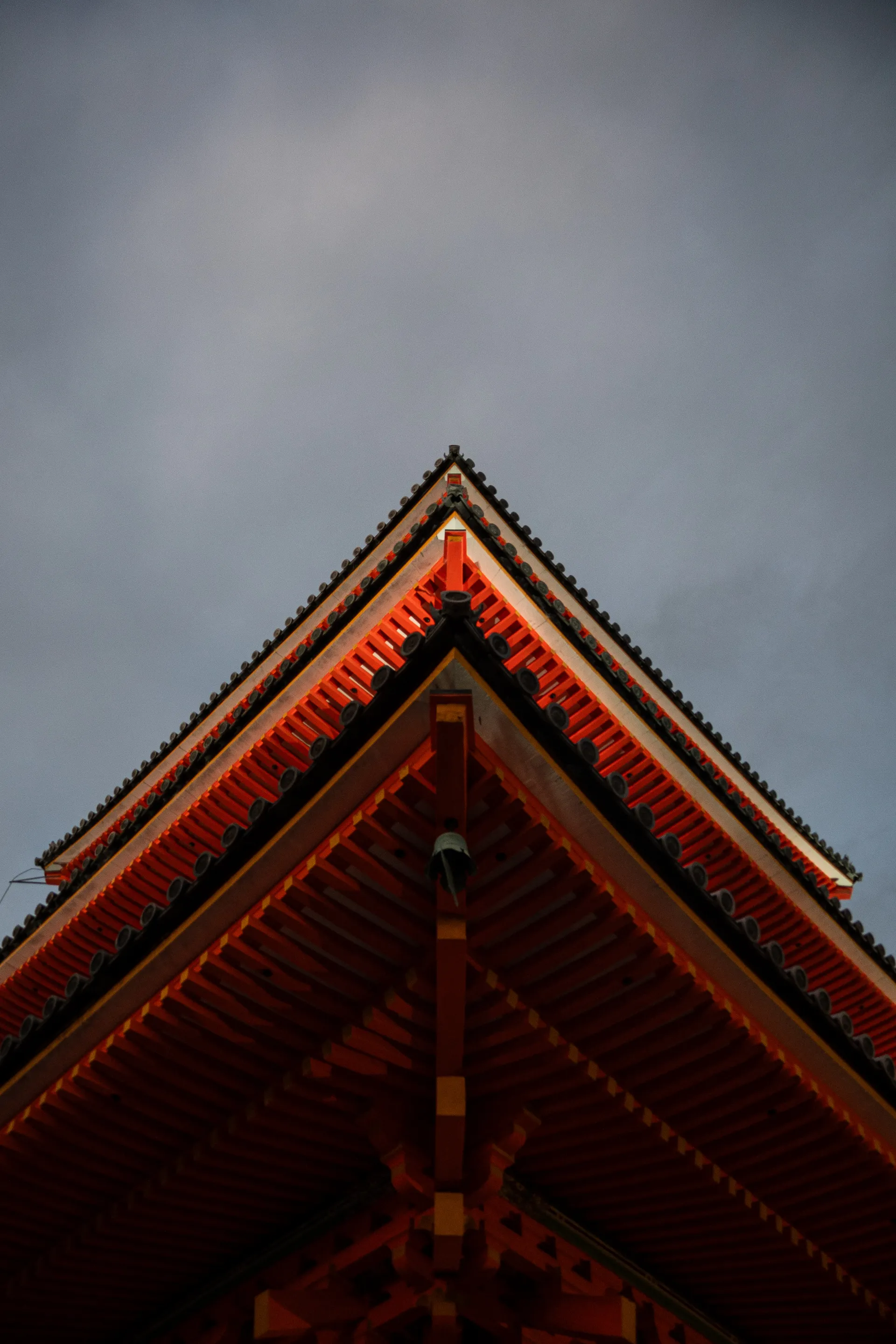The layered red roof of a traditional Japanese temple rises against a moody blue-gray sky.