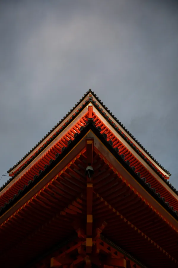 The layered red roof of a traditional Japanese temple rises against a moody blue-gray sky.