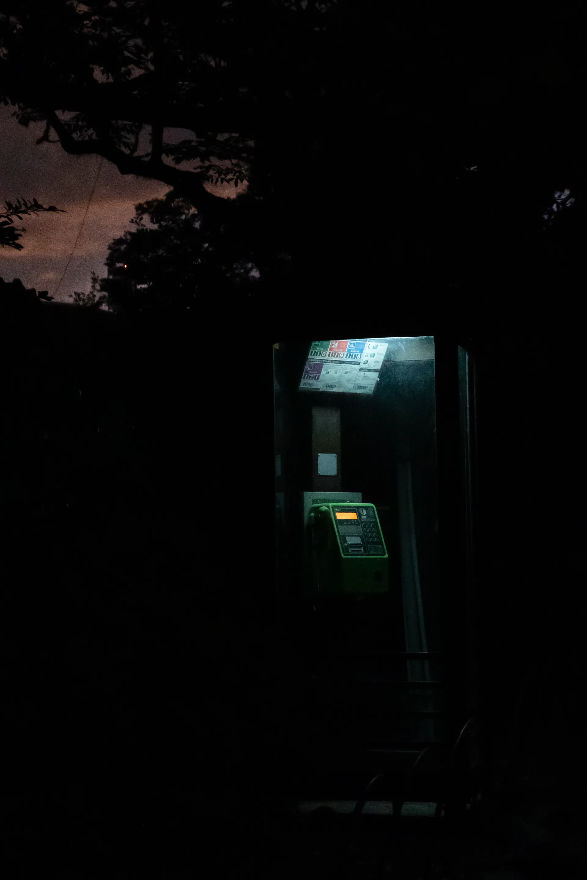 A green phone booth glows against the fading twilight sky.