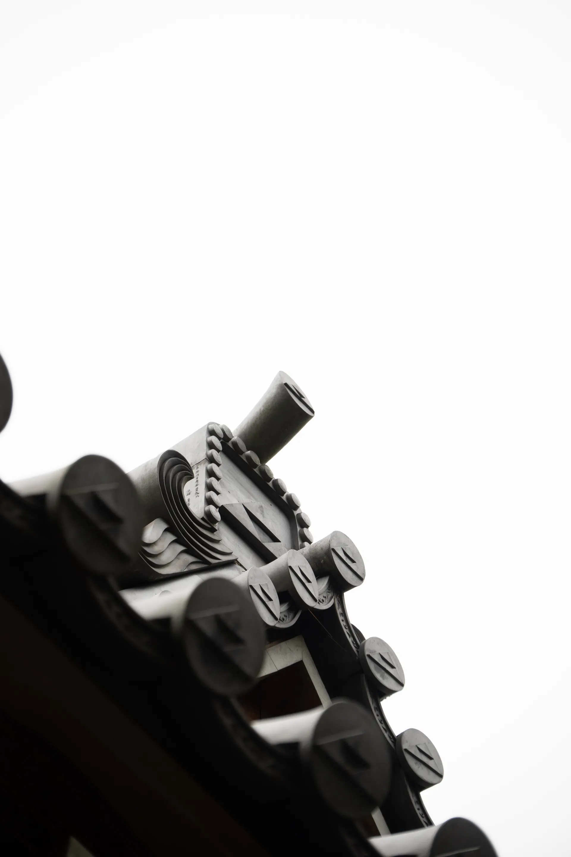 Cinematic view of traditional temple roof ornaments and cylindrical tiles rising against a pale sky.