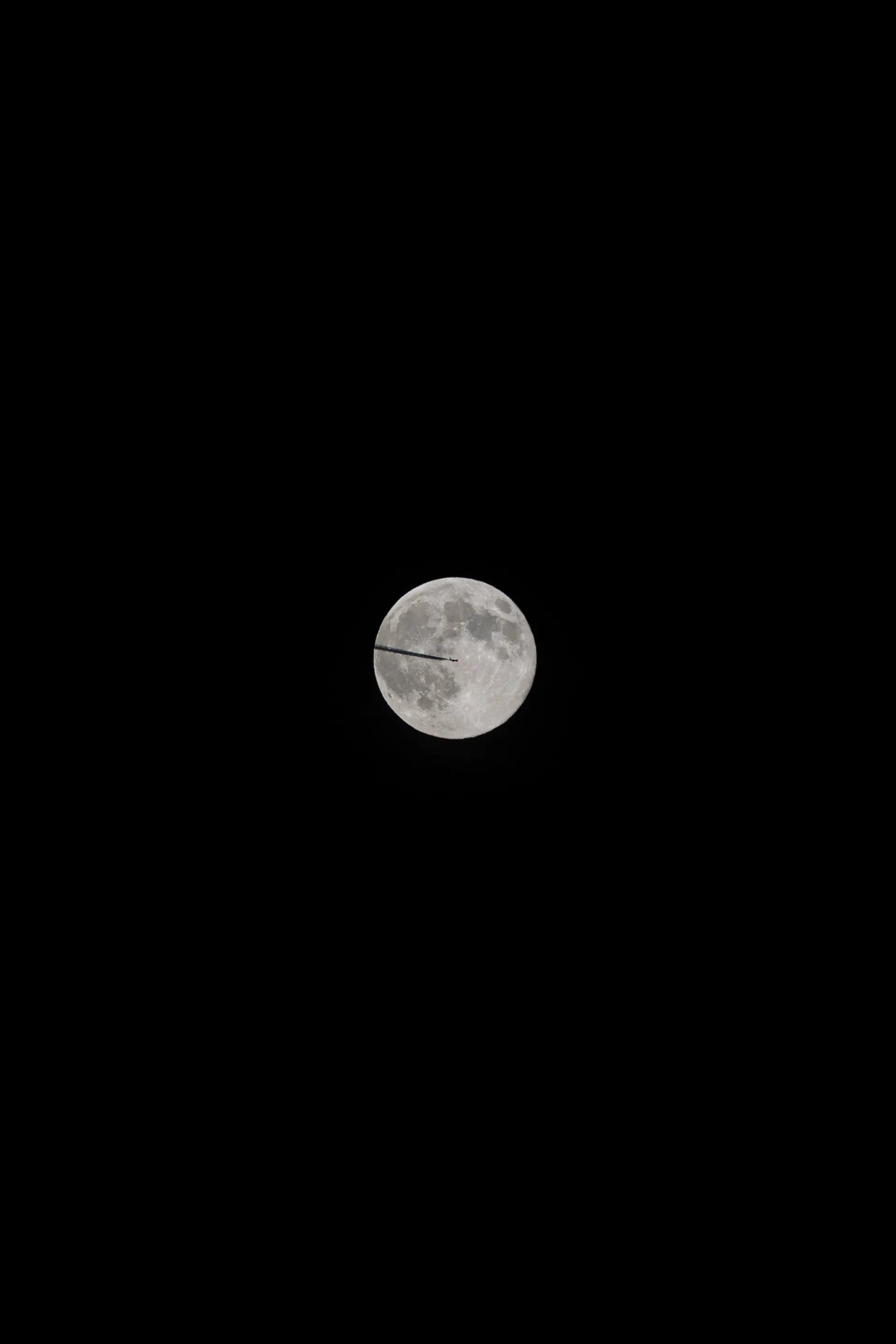 An airplane crosses the face of the full moon, a fleeting silhouette against the lunar surface.