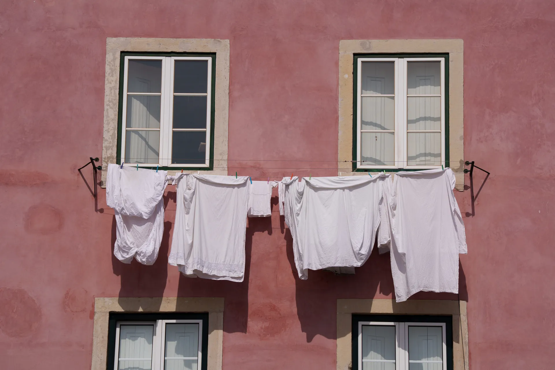 White laundry hangs on a line strung between two windows of a salmon-pink Lisbon facade.