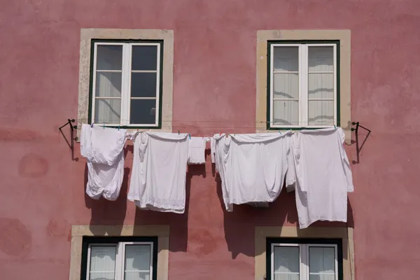 White laundry hangs on a line strung between two windows of a salmon-pink Lisbon facade.