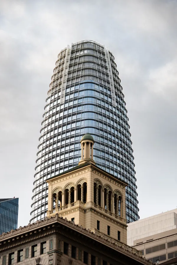 Salesforce Tower rises behind a historic stone building, contrasting San Francisco's past and present.