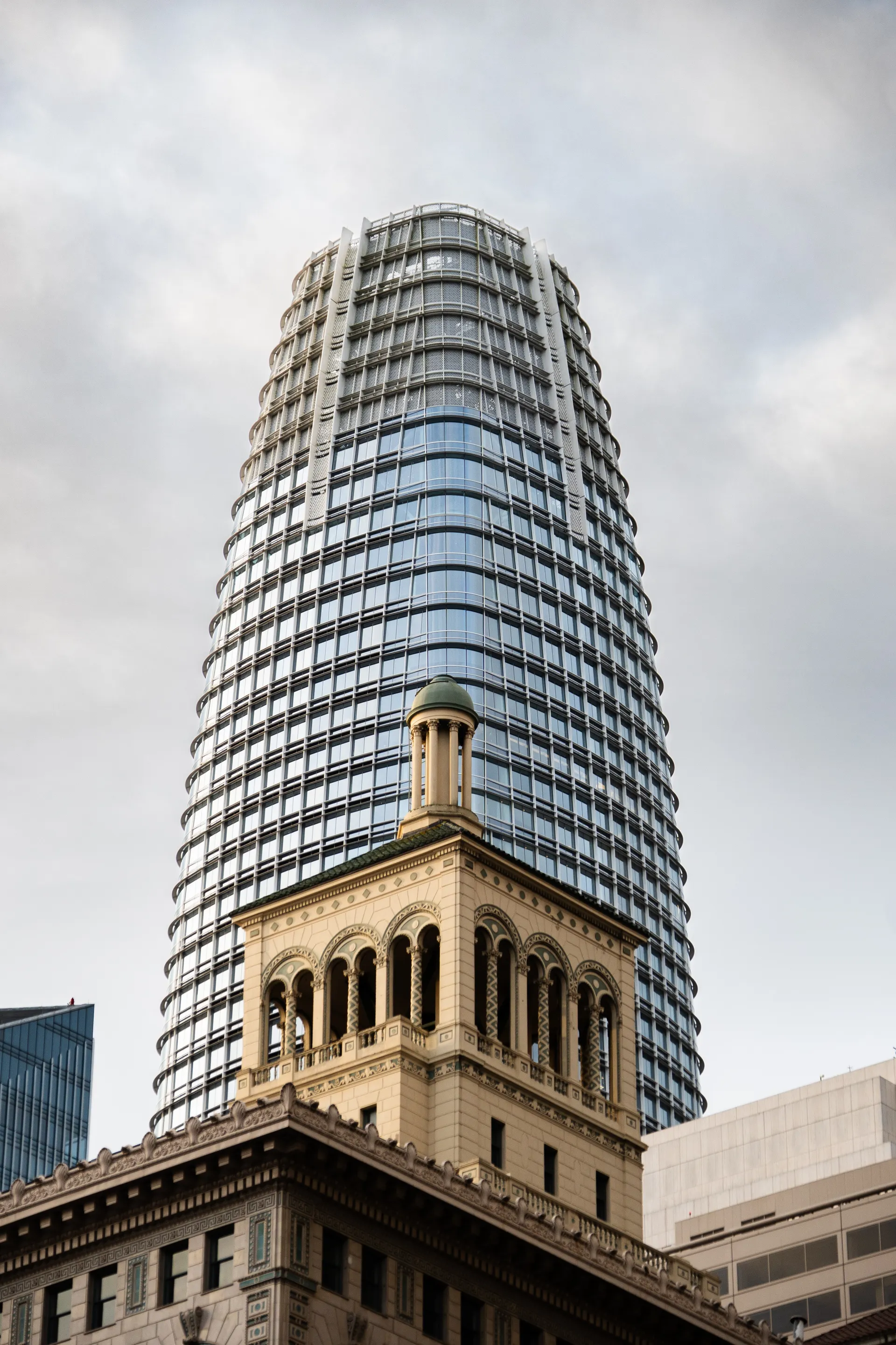 Salesforce Tower rises behind a historic stone building, contrasting San Francisco's past and present.