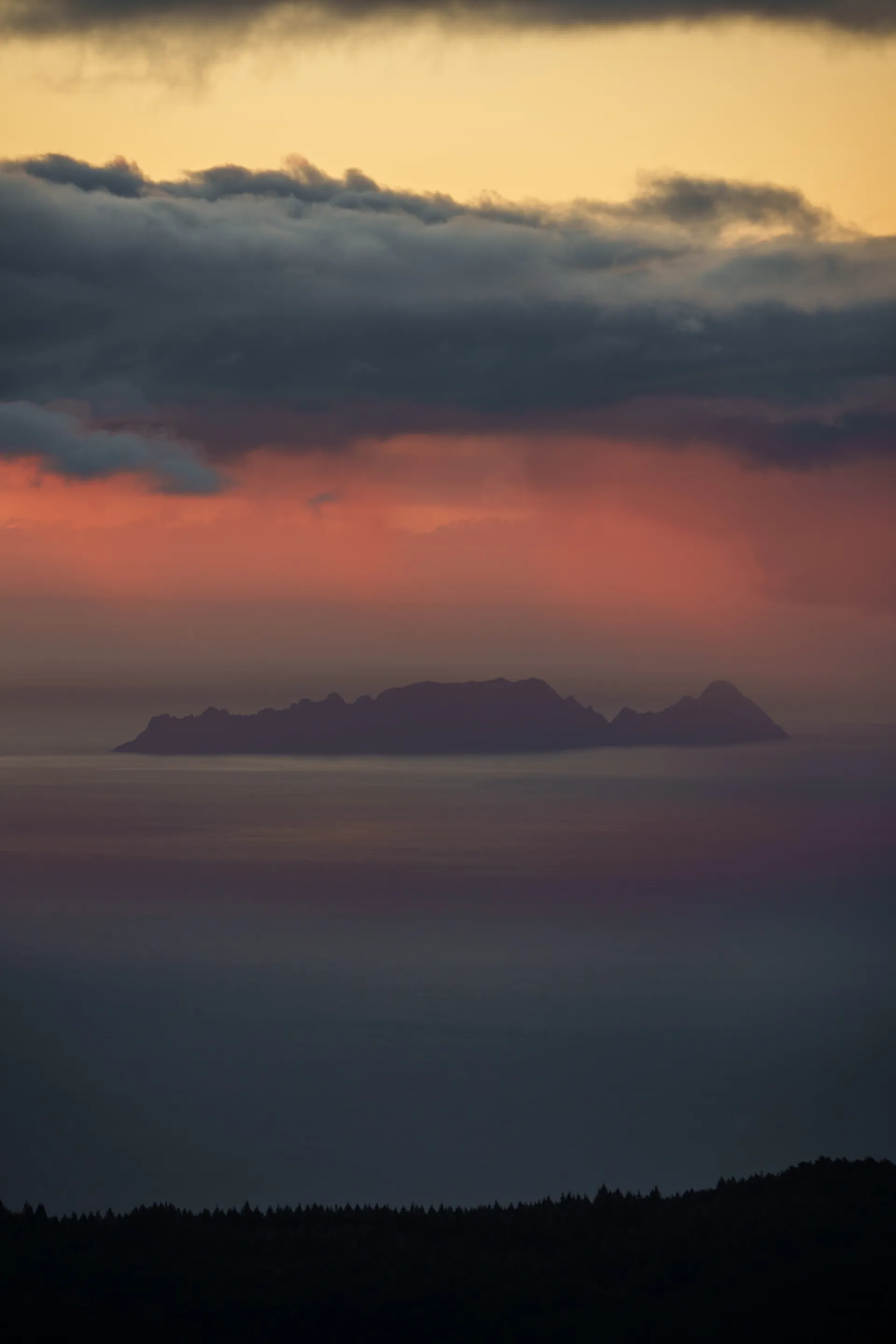 Island silhouettes emerge through layers of mist and fog beneath a dramatic sky painted in pink and gray tones.