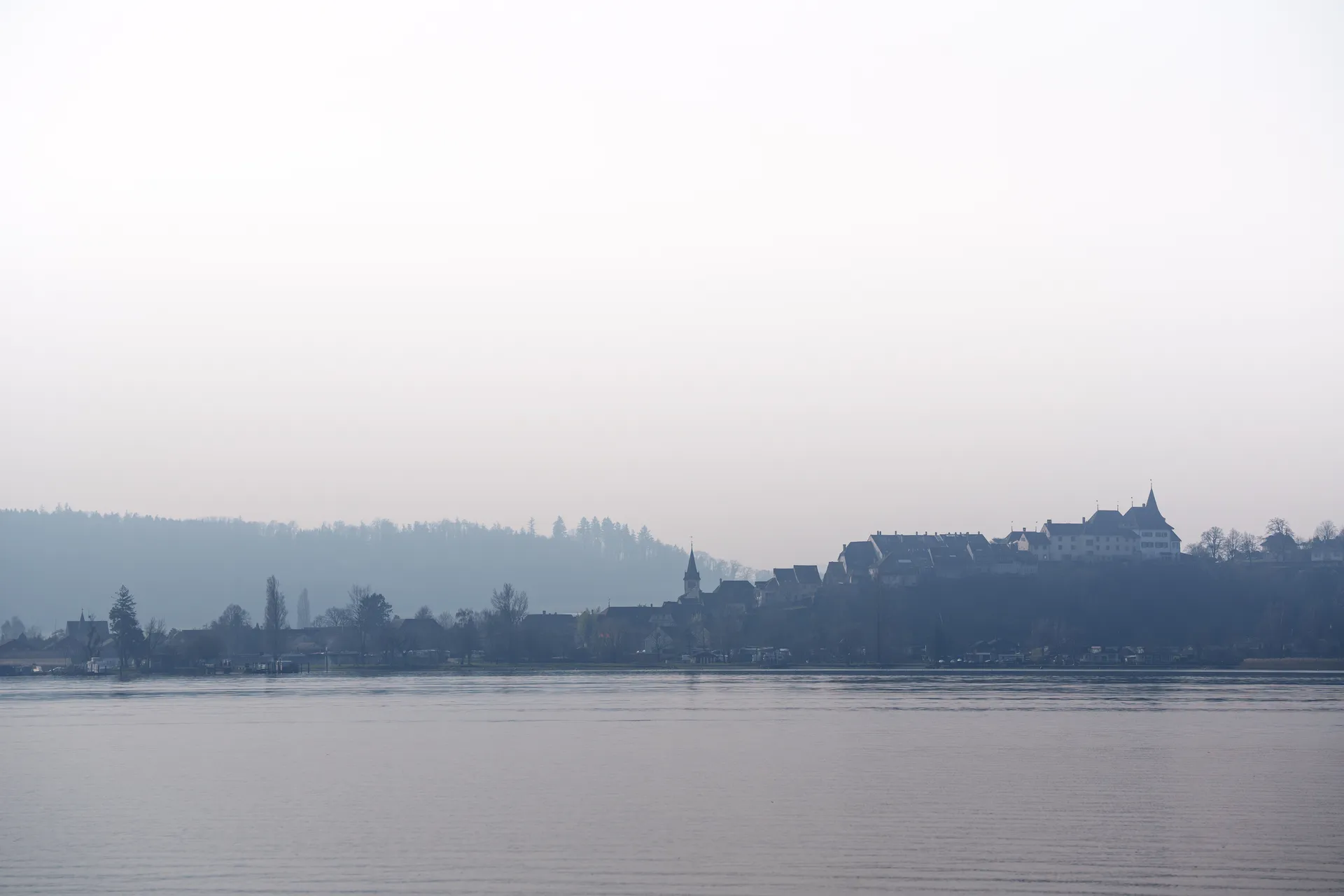 Erlach emerges from the mist across Lake Biel, its church steeple and hilltop castle barely outlined against layers of grey.