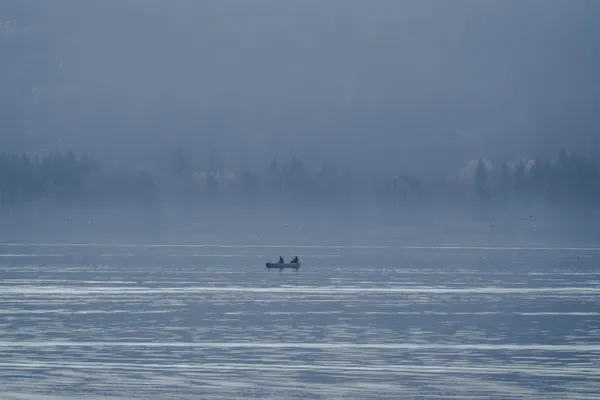 A lone fishing boat rests on a misty lake as birds cross the still morning air, movement flickering through a familiar childhood landscape.