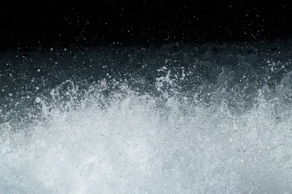 White water erupts against a dark background, frozen in mid-spray from an artificial waterfall.