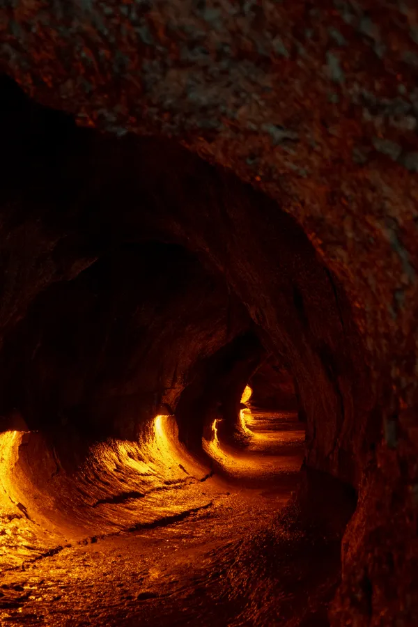 Light glows through an ancient lava tube, illuminating the textured walls carved by flowing molten rock.