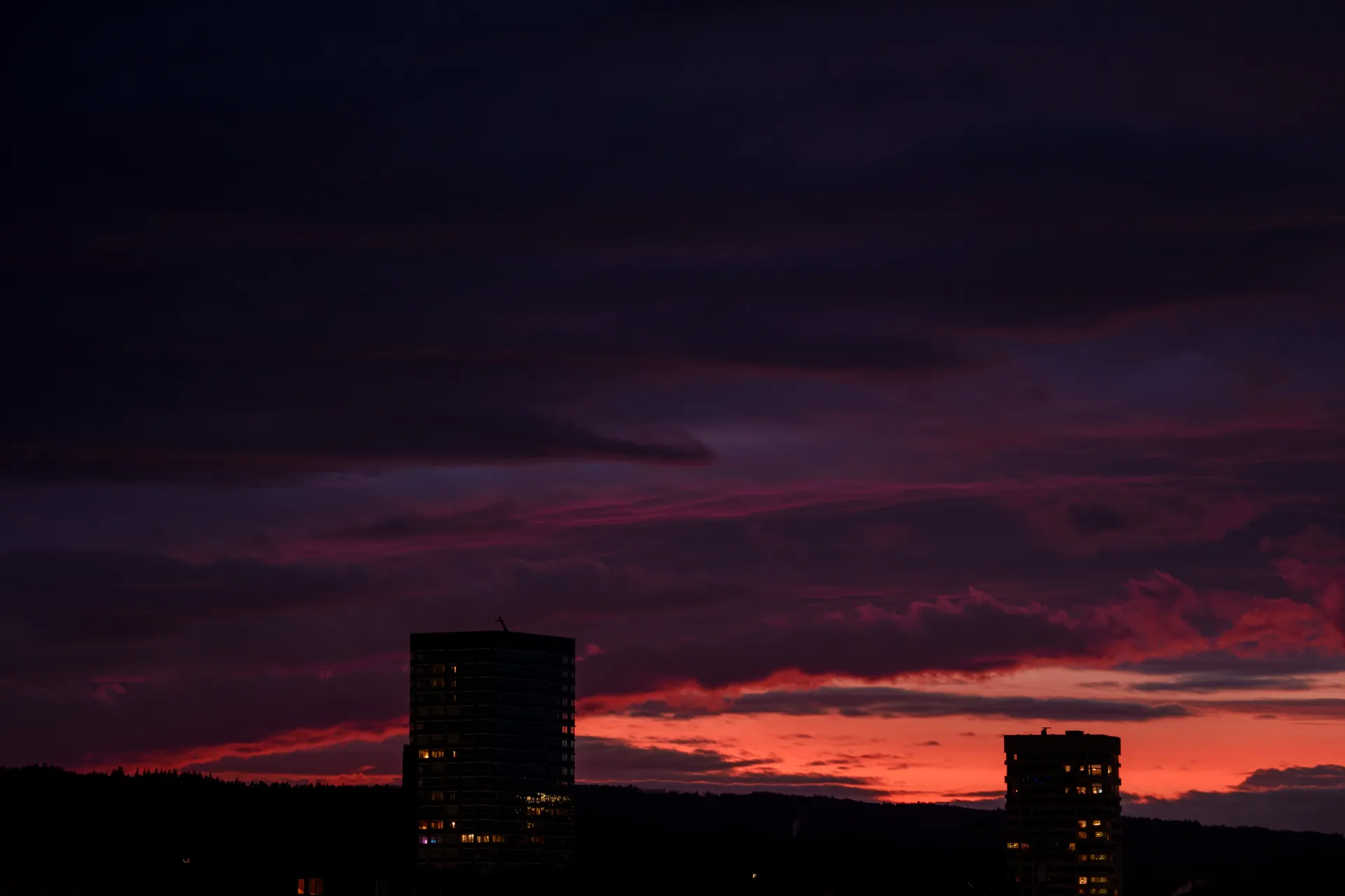 Two tower silhouettes stand against a vivid sunset sky layered in deep purple, pink, and fiery orange over the Zurich skyline.
