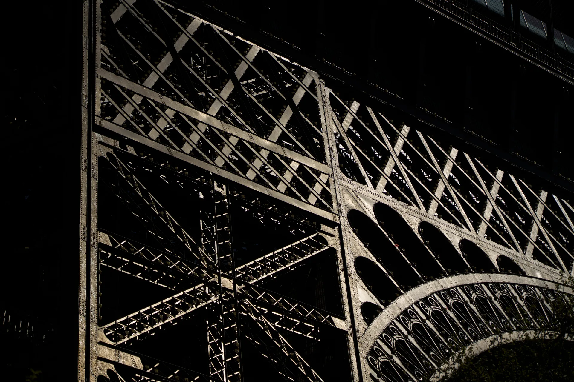 The Eiffel Tower's iron lattice catches low light, revealing the intricate geometry of its riveted arches.