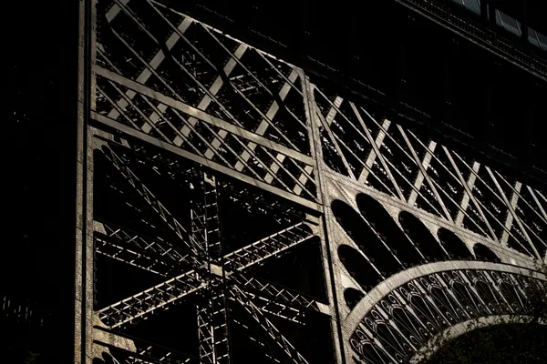The Eiffel Tower's iron lattice catches low light, revealing the intricate geometry of its riveted arches.