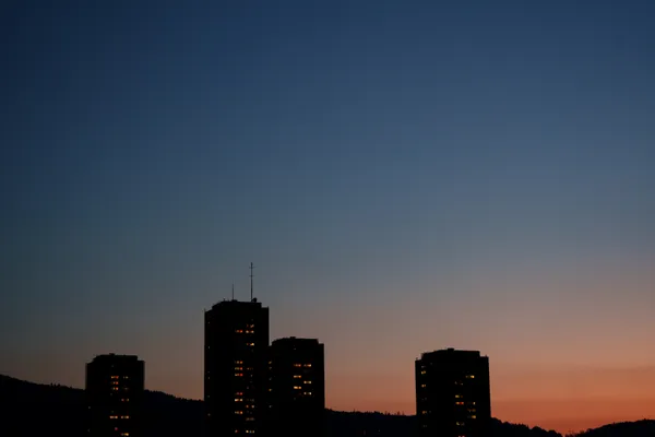 Apartment towers stand in silhouette against a deep blue-to-orange sunset gradient.