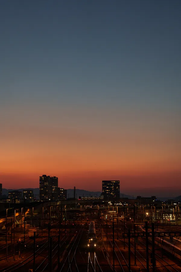 Railway lines converge beneath a warm sunset glow over the Zurich skyline.