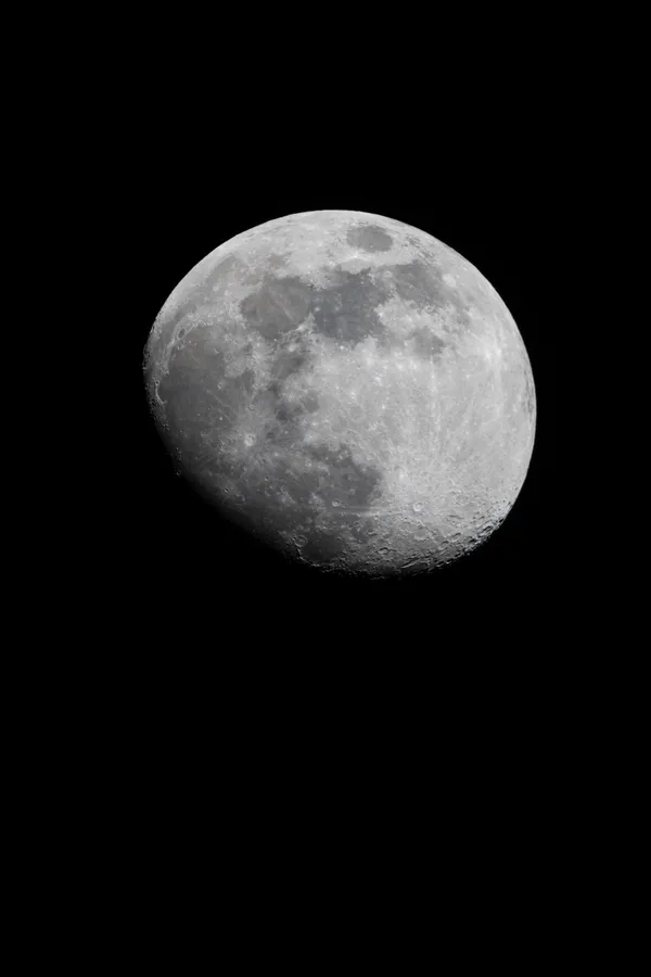 The moon hangs in the black night sky, its craters and maria sharply detailed across the illuminated surface.