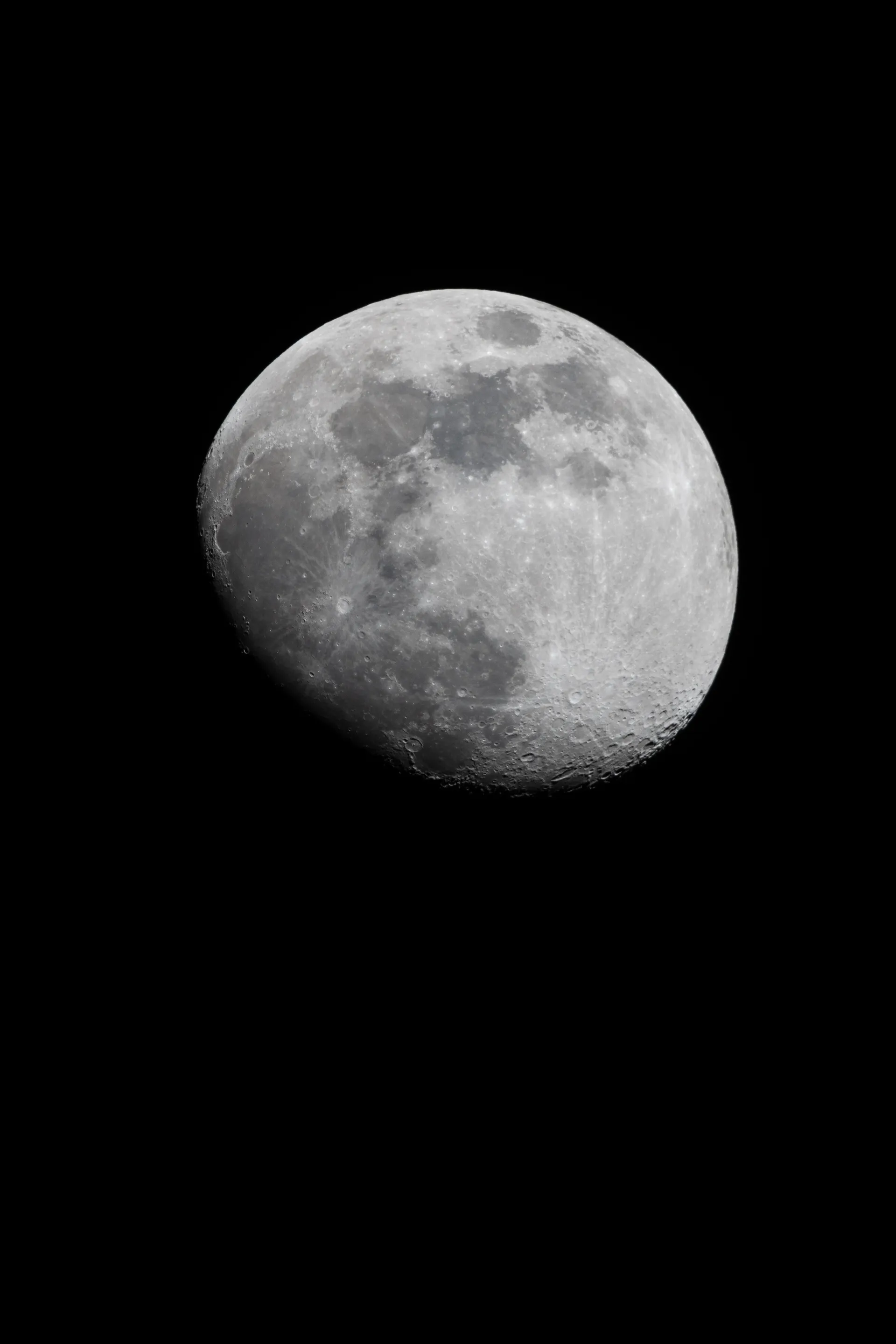The moon hangs in the black night sky, its craters and maria sharply detailed across the illuminated surface.
