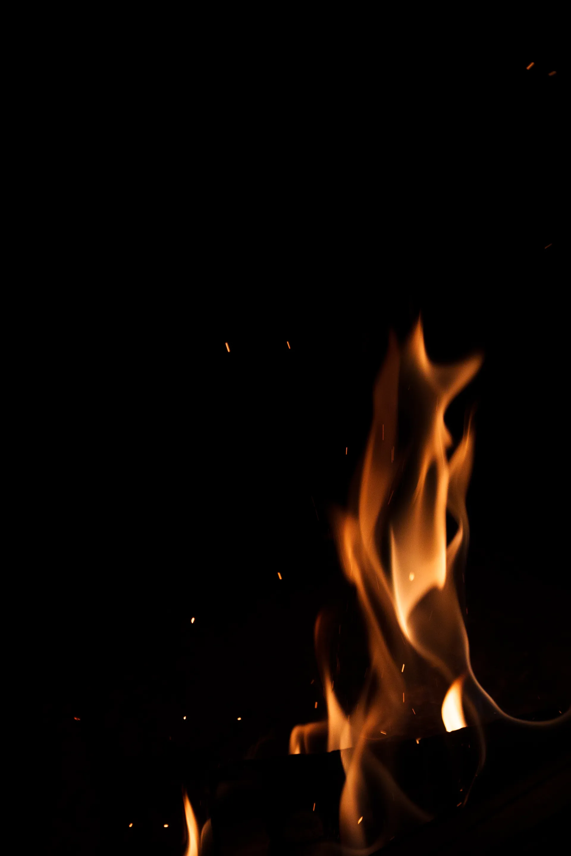 Flames dance and twist against the darkness, sparks drifting upward into the night.