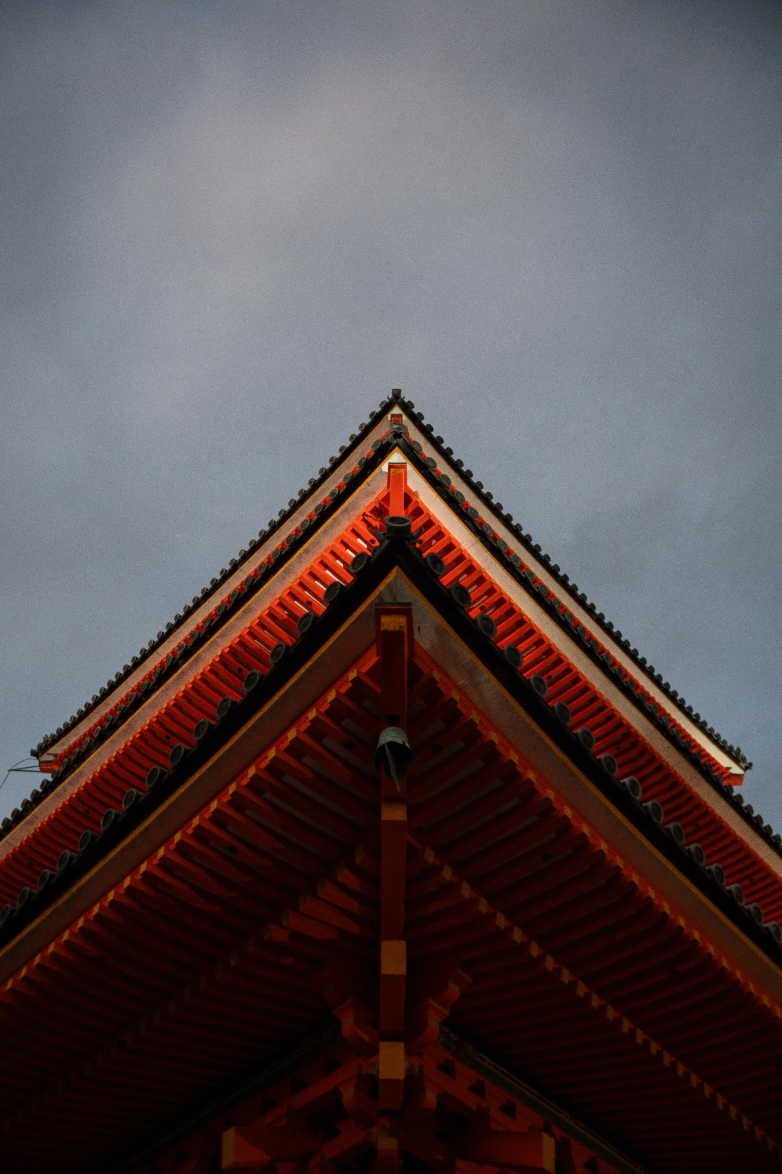 The layered red roof of a traditional Japanese temple rises against a moody blue-gray sky.