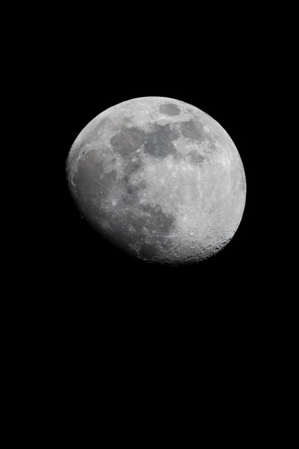 The moon hangs in the black night sky, its craters and maria sharply detailed across the illuminated surface.