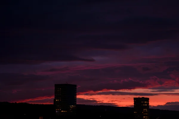 Two tower silhouettes stand against a vivid sunset sky layered in deep purple, pink, and fiery orange over the Zurich skyline.