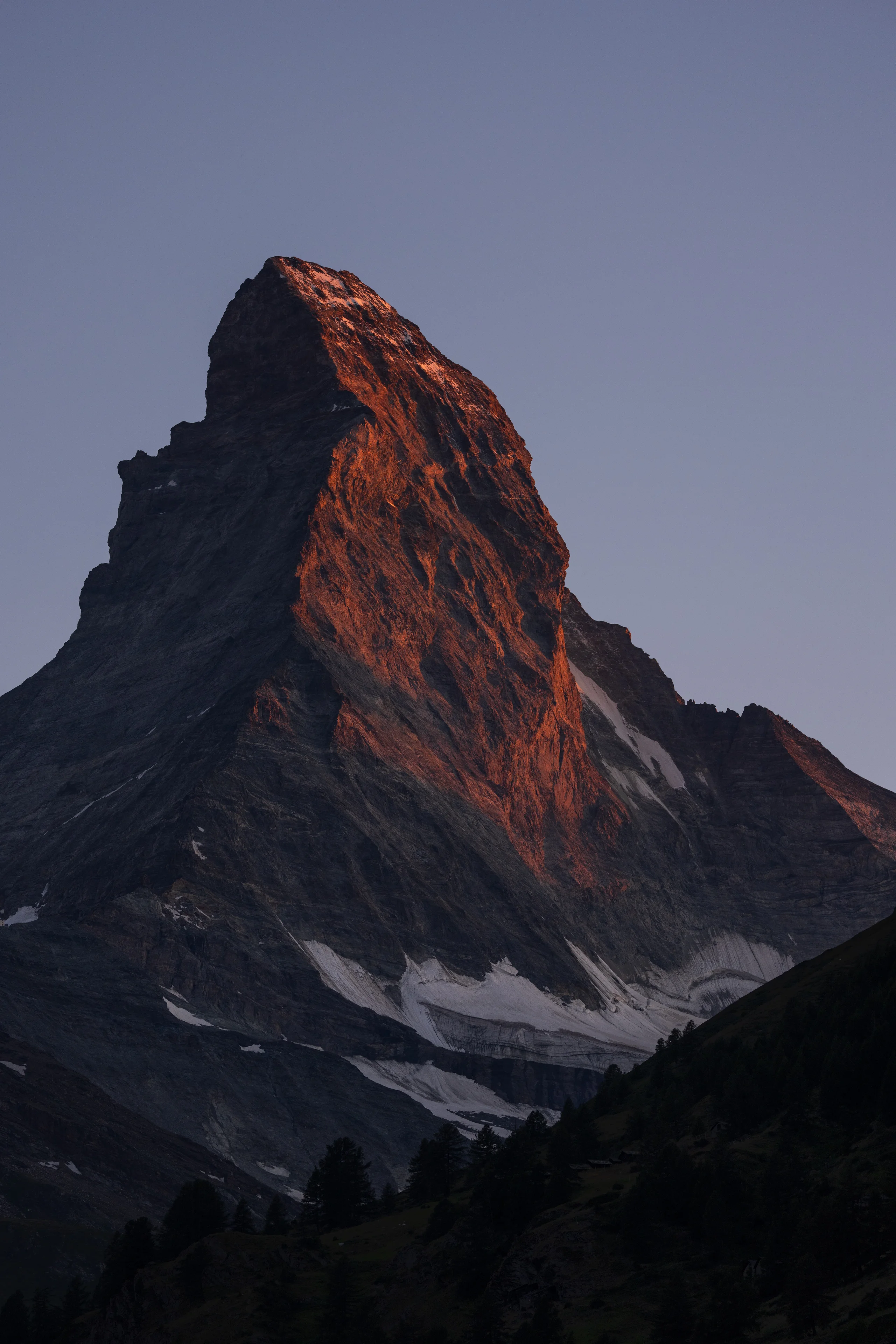 Warm alpenglow lights the upper face of the Matterhorn while its lower slopes and the surrounding valley rest in blue shadow.