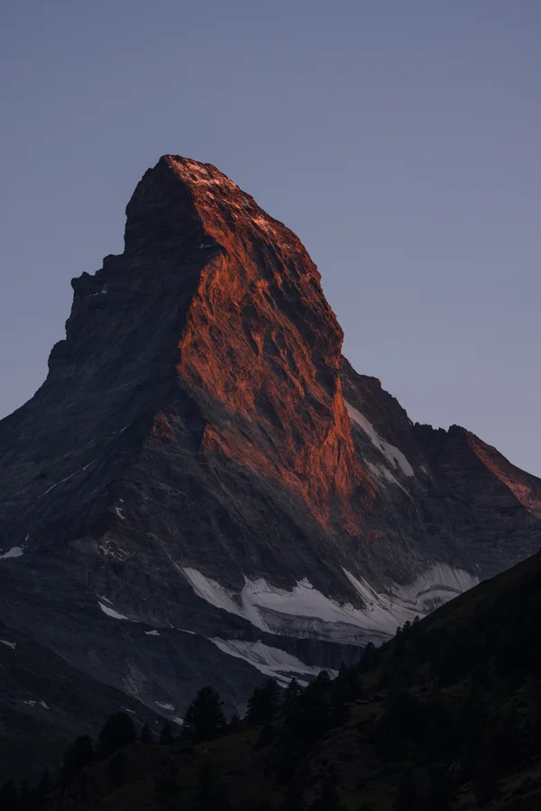 Warm alpenglow lights the upper face of the Matterhorn while its lower slopes and the surrounding valley rest in blue shadow.